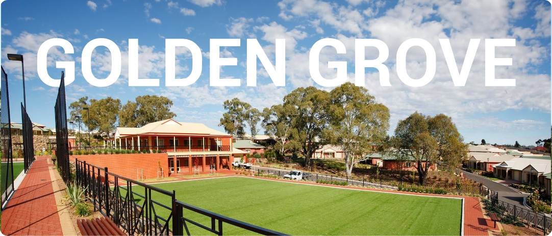 A landscaped area with a large green lawn surrounded by brick paths and buildings. The sky is partly cloudy. The words "GOLDEN GROVE" are overlaid in large white letters.