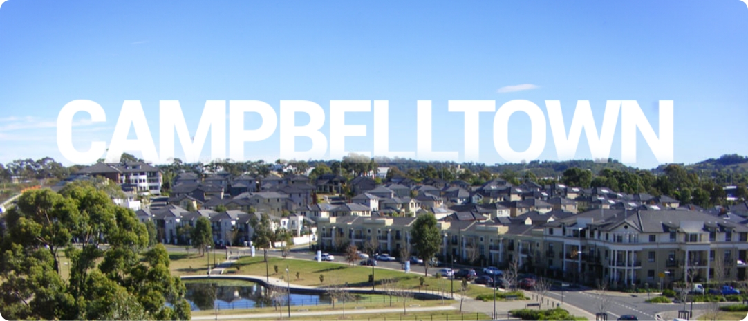 A scenic view of a suburban area with houses surrounded by trees under a clear blue sky. The word "CAMPBELLTOWN" is prominently displayed across the top in bold white letters.