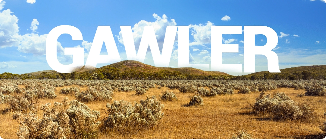 Dry landscape with sparse bushes under a bright blue sky and scattered clouds. The word "GAWLER" is prominently overlaid in white, large letters across the horizon.