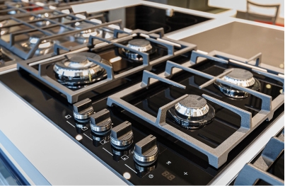 brand-new-gas-stoves-2024-10-17-23-34-42-utc Close-up of a modern black and stainless steel gas stovetop with four burners and control knobs, set on a shiny kitchen countertop.