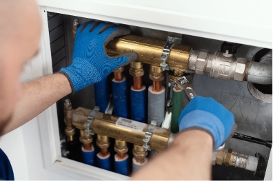professional-plumber-installing-plumbing-manifolds-2025-01-08-07-55-13-utc A person wearing blue gloves uses a wrench to tighten a brass pipe fitting in a plumbing system with multiple pipes and connectors inside a metal cabinet.