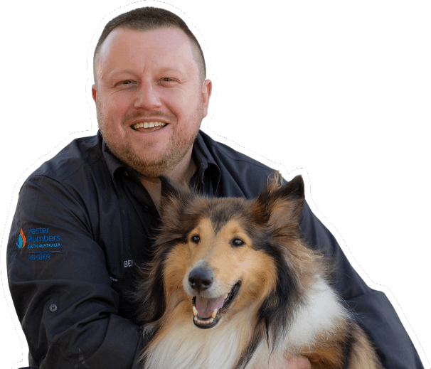A smiling man in a dark shirt hugs a happy, fluffy Collie dog. Both are looking at the camera against a plain white background.